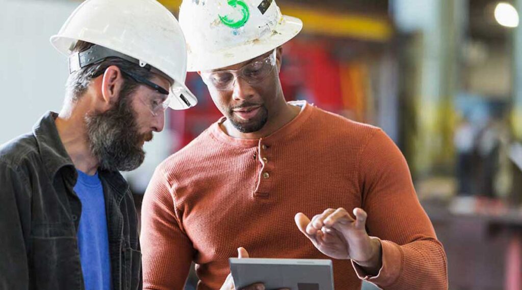 Two men in hardhats looking at a tablet device