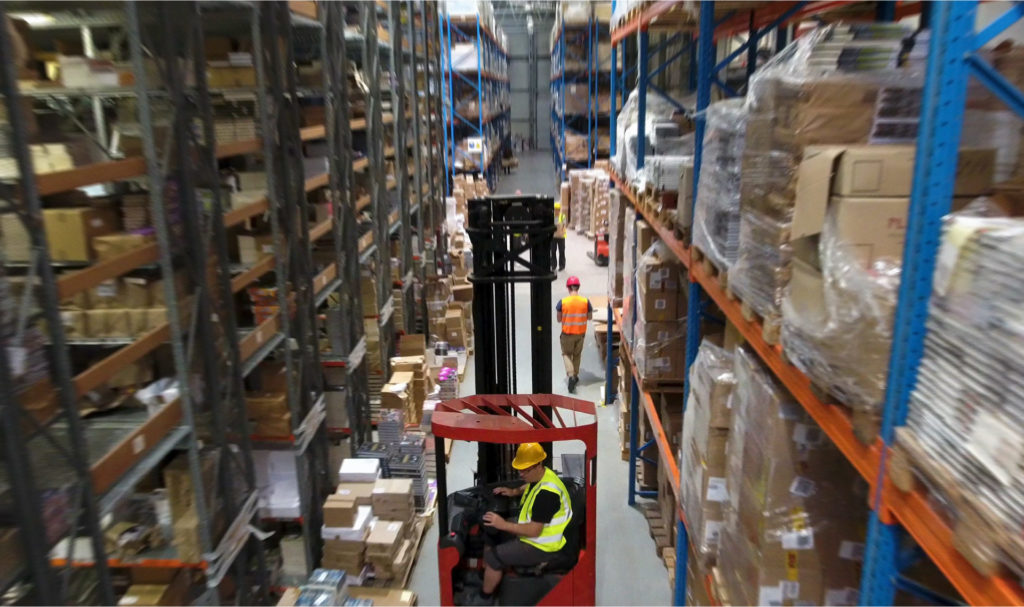 A forklift being driven down an aisle in a warehouse.