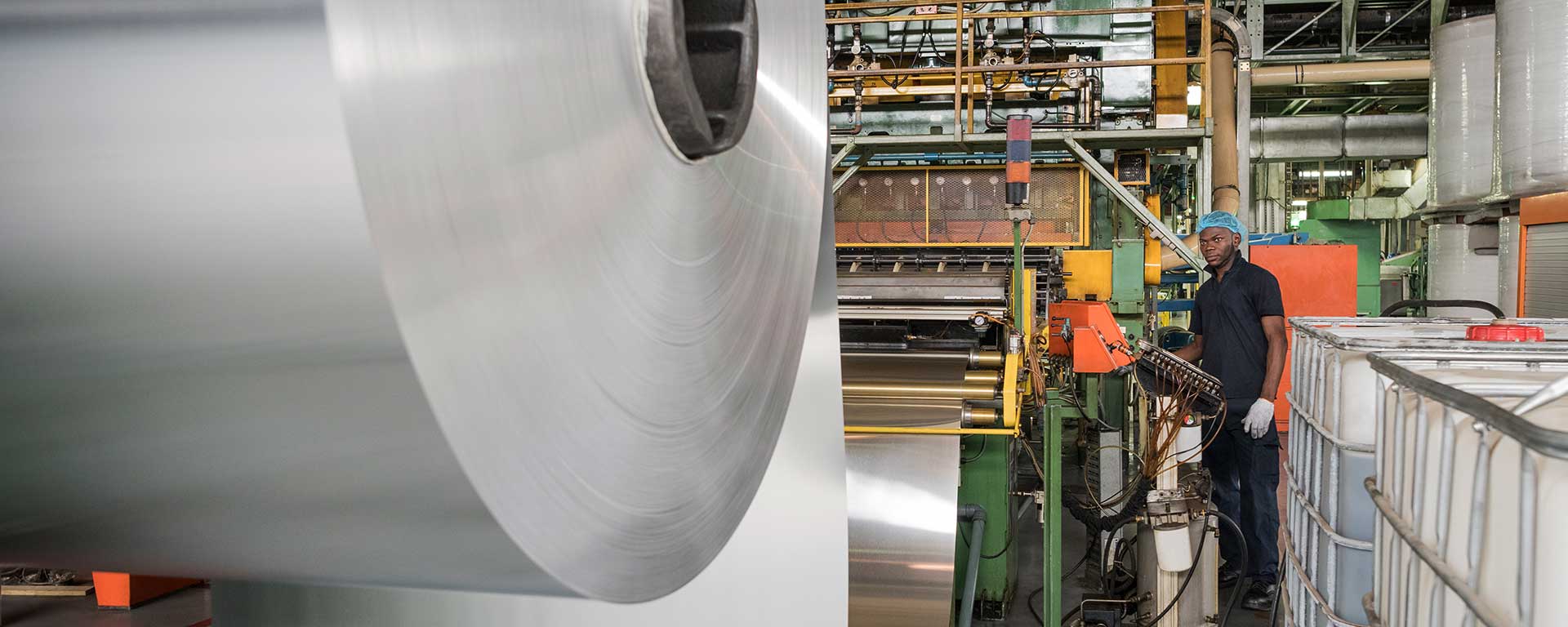 Worker observes roll of sheet metal in factory