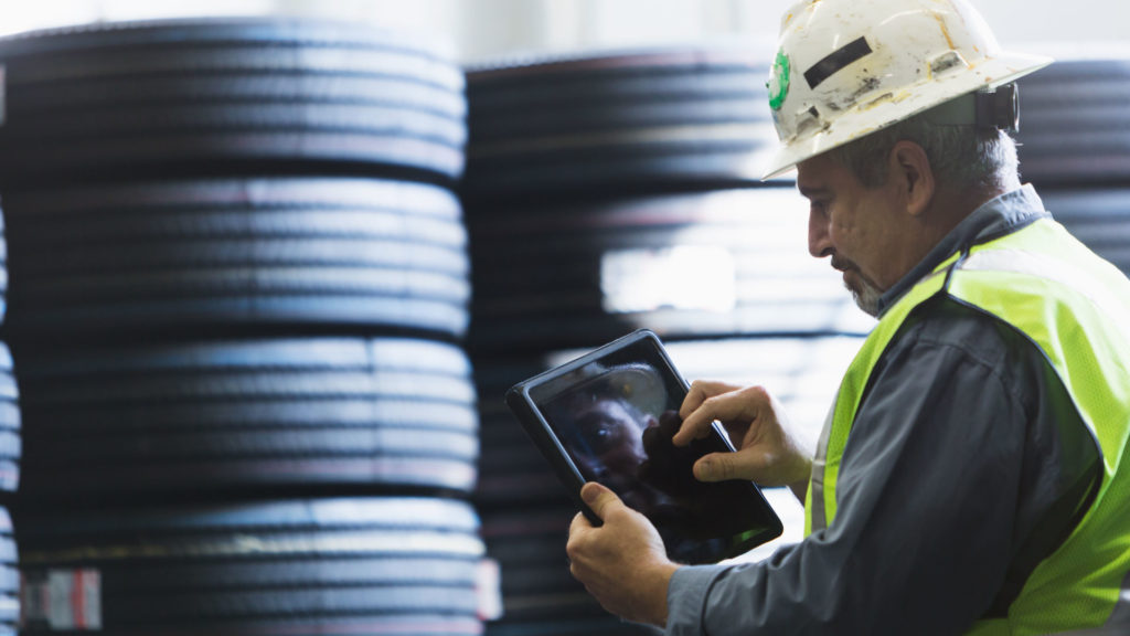 A man using a tablet device in front of a stack of tires.