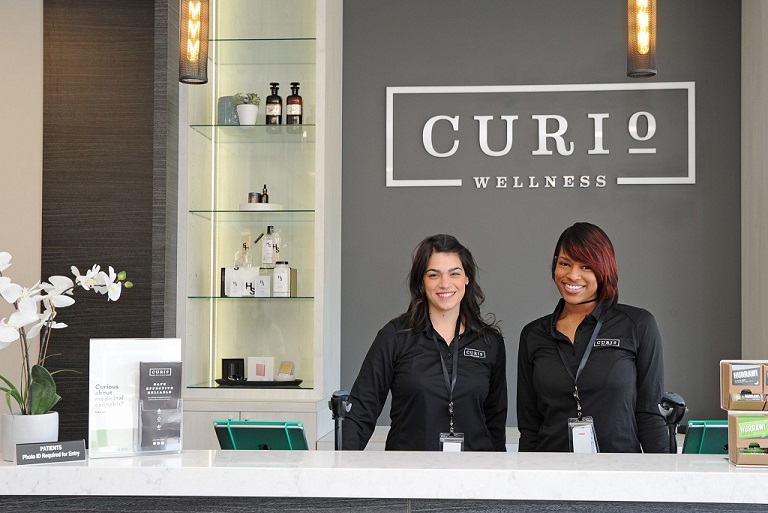 Two Curio Wellness employees standing behind the front desk and smiling at the camera
