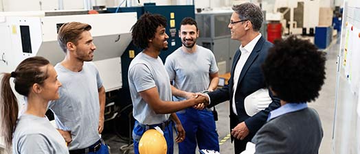 A man in a suit shaking the hands of factory workers