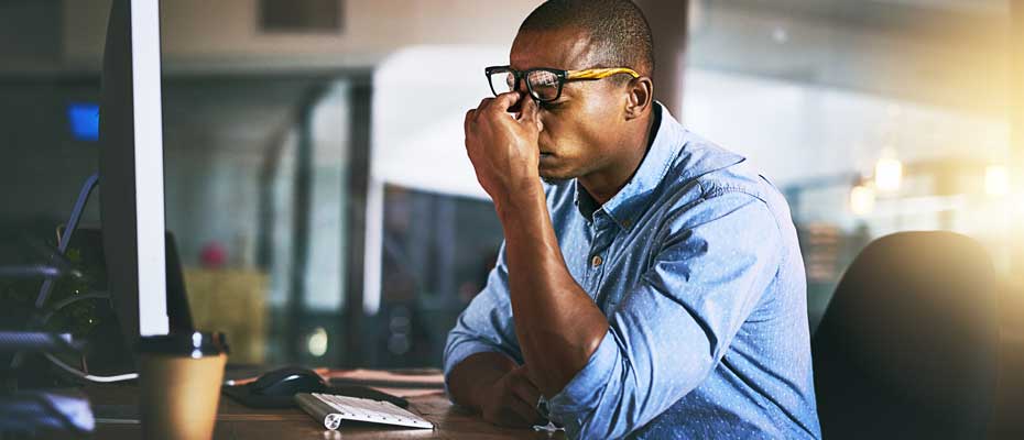 A man pinching the bridge of his nose in frustration at his desk