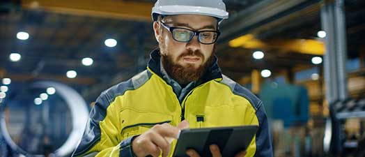 A man in a hardhat in a factory using a tablet device.