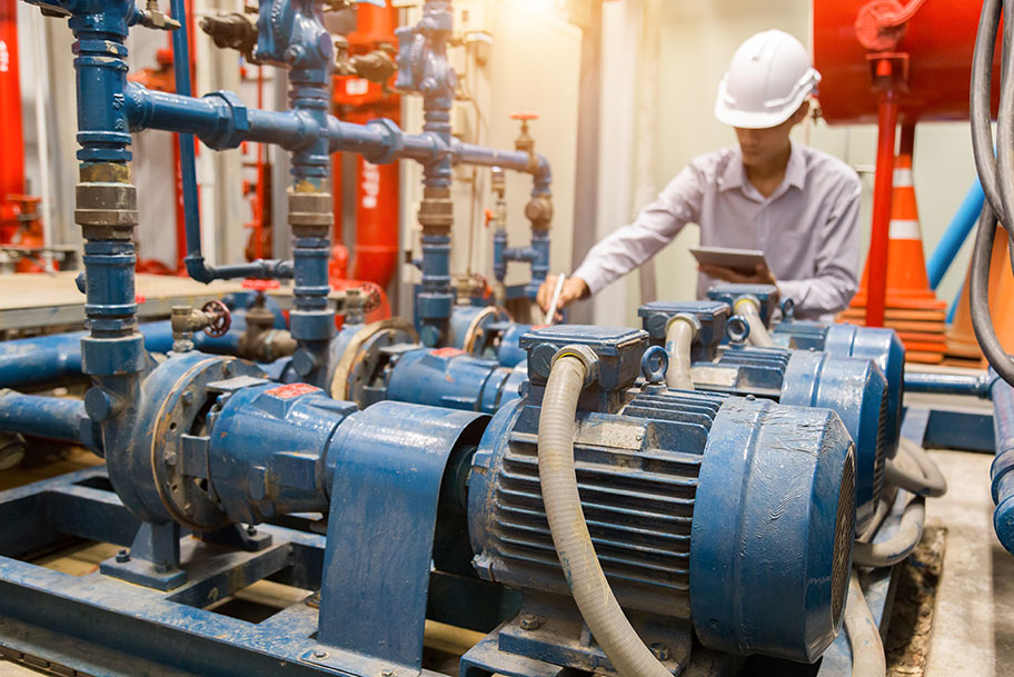 A man inspecting industrial pumps and holding a tablet device.