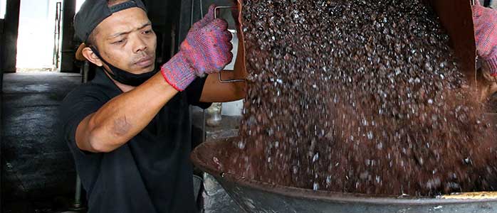 A man pouring coffee beans into machinery.